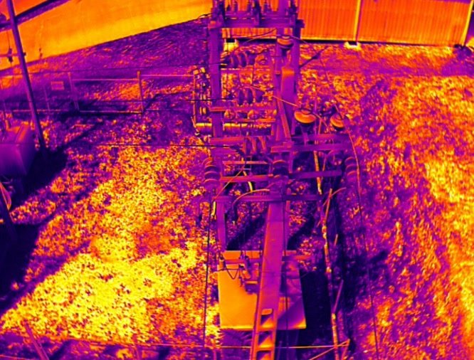 Aerial thermal image of a 33 kV gantry and switchyard showing conductors, insulators and steelwork against sun-warmed ground