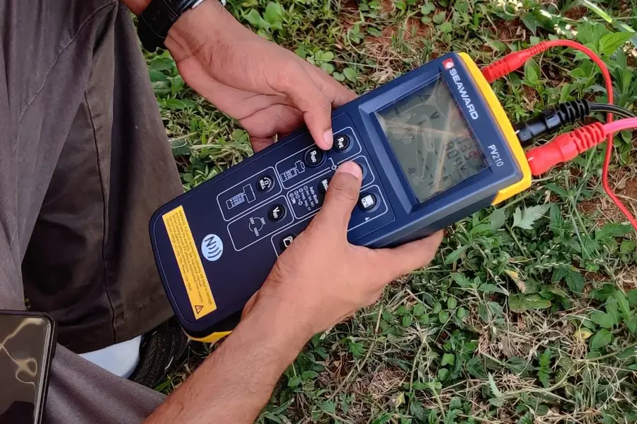 Solar Pv Consultancy 8 Vibhawa engineer running a string test on a Seaward PV210 solar installation tester beside a ground-mounted array