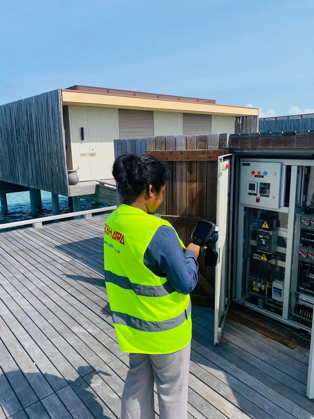 Vibhawa thermographer scanning an overwater villa electrical panel at Patina Maldives